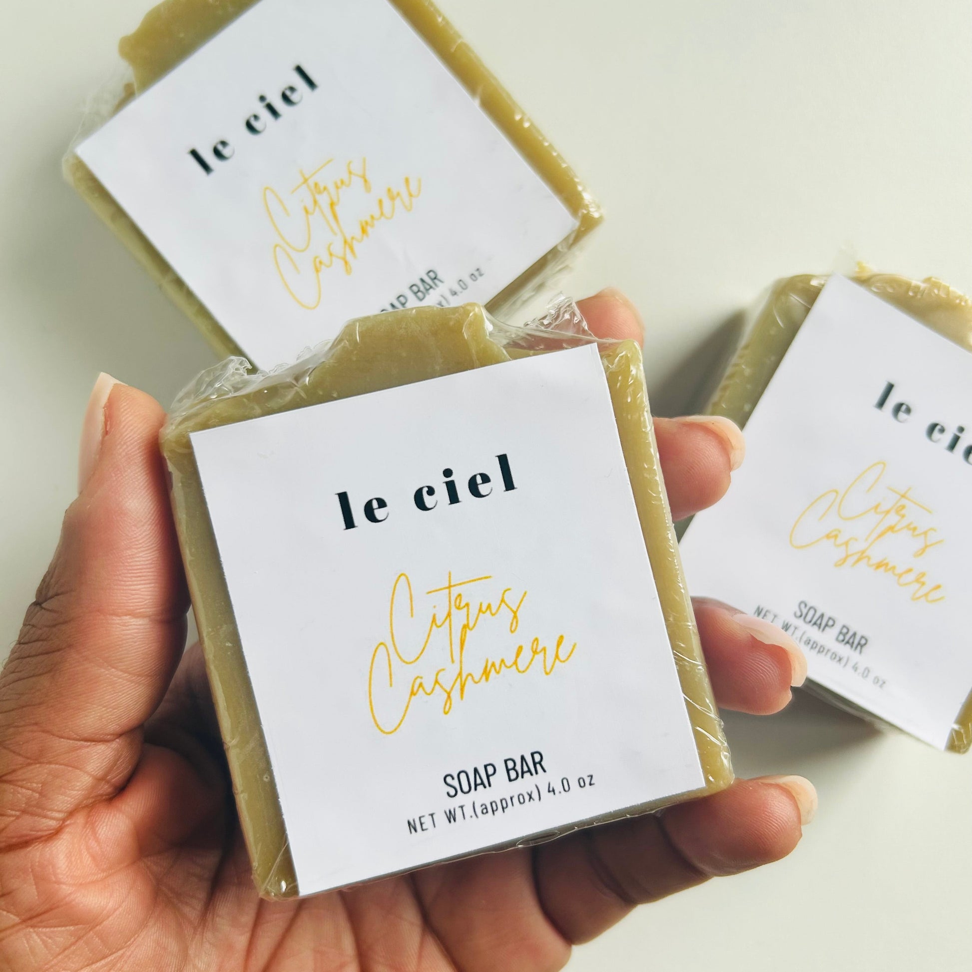 Hand holding a soap bar labeled 'le ciel' with another soap bar in the background.